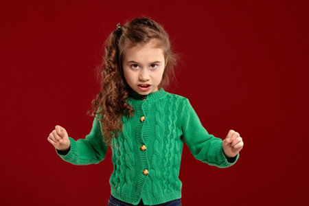 Portrait of a little brunette girl with a long, curly hair posing against a red background.の写真素材