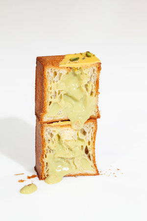 Cut in half fluffy cube shaped croissant with pistachio cream and nut crumbs