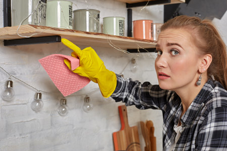 Woman in gloves cleaning furniture with rag at home kitchen.