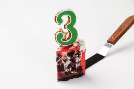 Slice of chocolate cake with glazed cookie in shape of number threeの写真素材