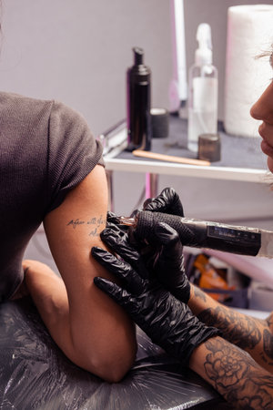 Professional tattoo artist using machine to etch inscription on female armの写真素材