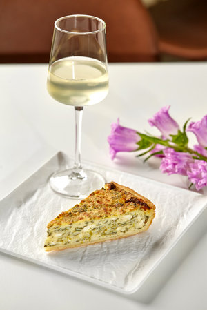 Piece of cheese and spinach quiche with wine and flowers