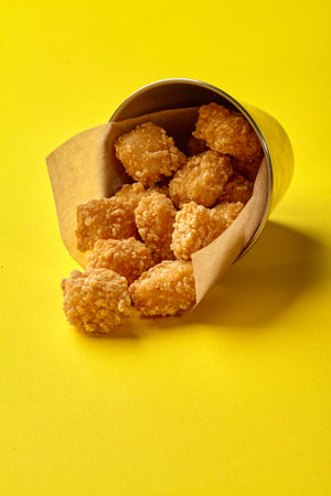 Crispy fried chicken nuggets spilling from metal bucket on yellowの写真素材