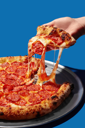 Hand taking a slice of delicious pepperoni pizza with melted cheese