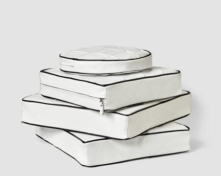 Stack of stylish white leather cushions with black piping on plain backgroundの写真素材