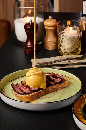 Delicious beef bruschetta with poached egg and cheese sauce being poured on topの写真素材