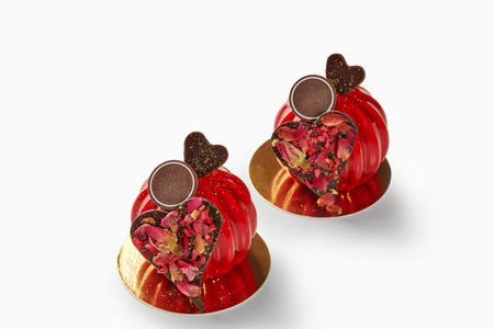 Two red mousse cakes decorated with chocolate hearts and rose petals for valentines dayの写真素材
