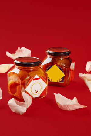 Two luxardo baba al maraschino jars decorated with rose petals on red background