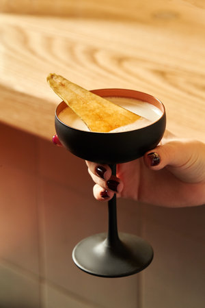 Woman holding a coupe glass with a cocktail and a garnishの写真素材