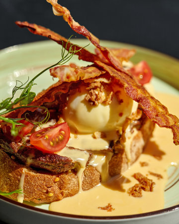 Gourmet breakfast or brunch with eggs benedict, bacon, hollandaise sauce, and cherry tomatoes on toasted breadの写真素材