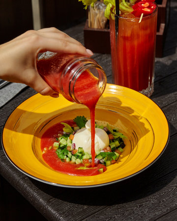 Chef pouring tomato soup on burrata cheese with vegetable salad in yellow plateの写真素材