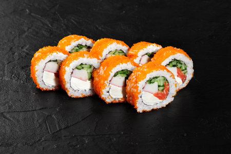 uramaki rolls covered with tobiko flying fish roe lying on black slate surfaceの写真素材