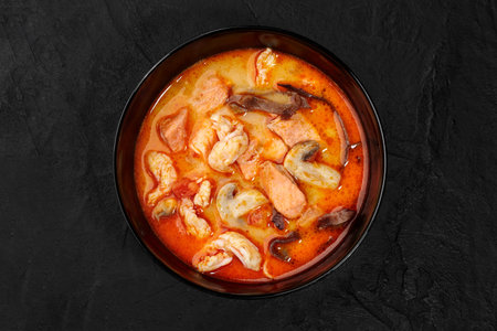 Tom yam soup with salmon, shrimp, and mushrooms in black bowlの写真素材