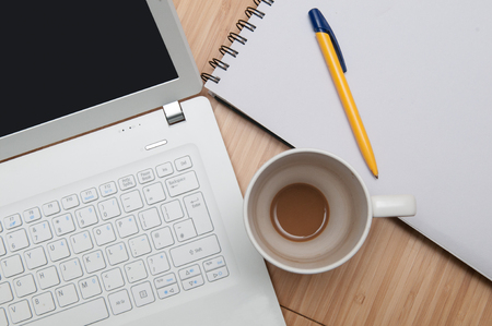 Laptop and notepad on the table with an empty coffee cupの写真素材