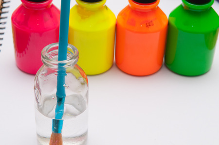 Paint brush in water in front of brightly coloured childrens paint pots for a rainy day activityの写真素材