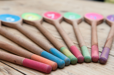 Brightly colored wooden spoons with numbers in a sequence arranged in a row on a wooden tableの写真素材