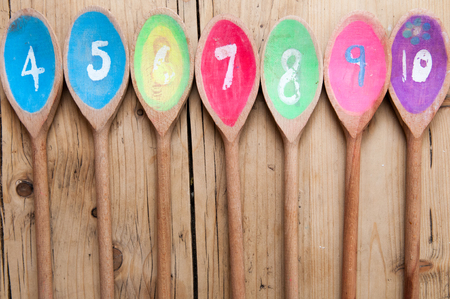 Brightly colored wooden spoons with numbers in a sequence arranged in a row on a wooden tableの写真素材