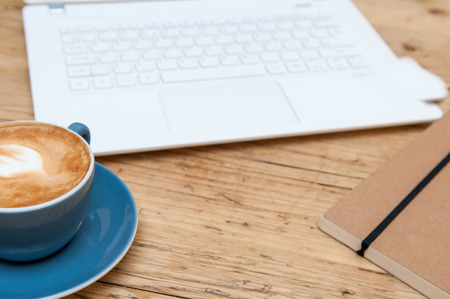 Fresh cup of coffee and laptop computer on a wooden table background in the cafeの写真素材