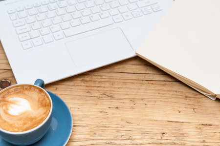 Fresh cup of coffee and laptop computer on a wooden table background in the cafeの写真素材