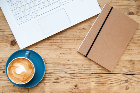 Fresh cup of coffee and laptop computer on a wooden table background in the cafeの写真素材