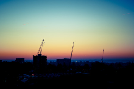 Cityscape sunrise with three construction work cranes silhouettedの写真素材