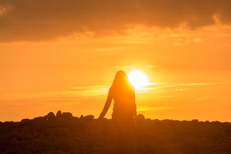 Young woman walks alone into the sunset at the beachの写真素材