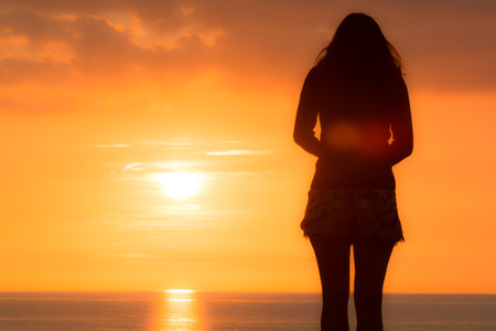 Young woman stands looking out to sea at the sunsetの写真素材