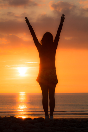 Woman at the beach reaches up in the sunsetの写真素材