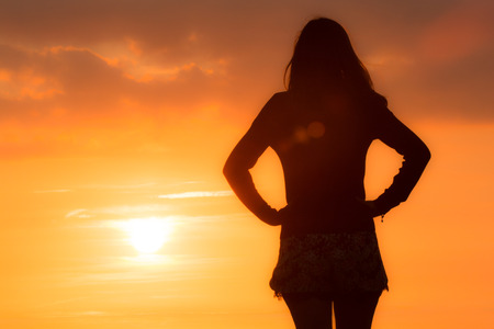 Young woman stands looking out to sea at the sunsetの写真素材