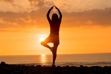 Woman practising Yoga at sunset on the beachの写真素材