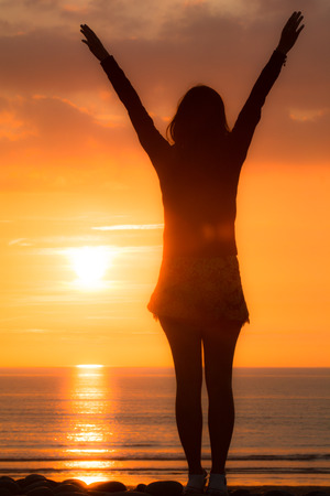 Woman at the beach reaches up in the sunsetの写真素材