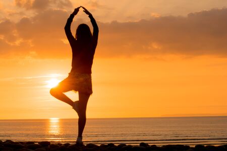 Woman practising Yoga at sunset on the beachの写真素材