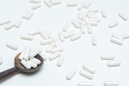 White tablets on a medicine dose spoon, with tablets across the tableの写真素材