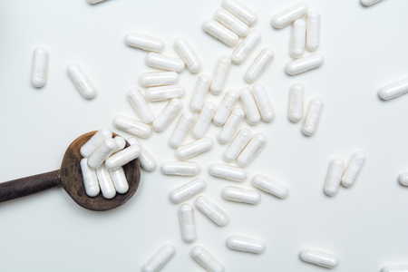 White tablets on a medicine dose spoon, with tablets across the tableの写真素材