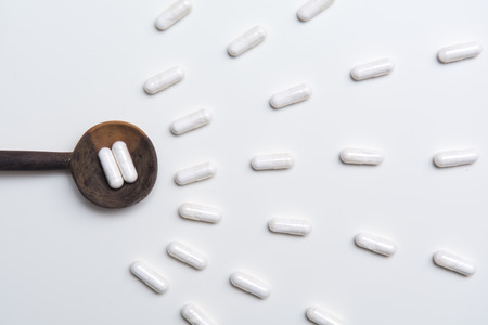 White tablets on a medicine dose spoon, with tablets across the tableの写真素材