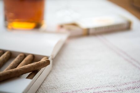 Cigars and whiskey on a light table cloth, one cigar out of the packetの写真素材