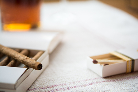 Cigars and whiskey on a light table cloth, one cigar out of the packetの写真素材