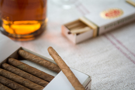 Cigars and whiskey on a light table cloth, one cigar out of the packetの写真素材