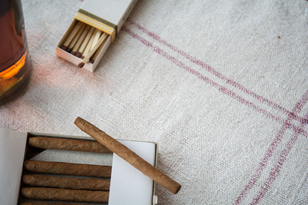 Cigars and whiskey on a light table cloth, one cigar out of the packetの写真素材