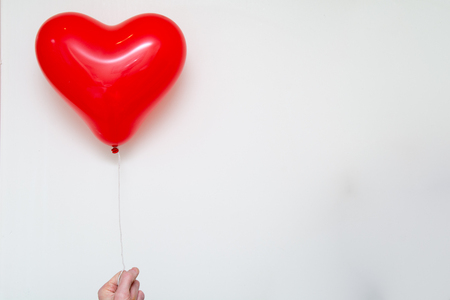 Hand holding a red heart balloon on a white backgroundの写真素材