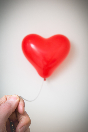 Male hand holding a red heart shaped balloonの写真素材