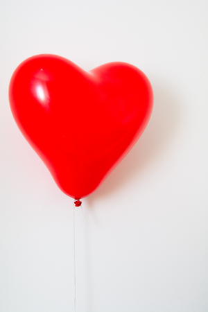 Red heart shaped balloon on a string isolated on whiteの写真素材