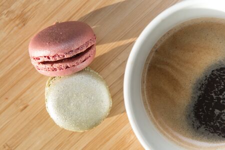 Coffee and macaroons on wooden table in sunlightの写真素材