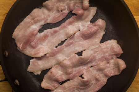 Streaky bacon cooking in the frying panの写真素材