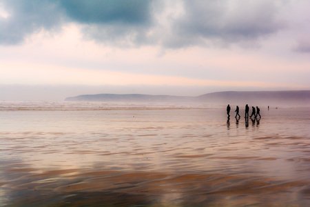 Group of people walking on a sandy beach in wet weatherの写真素材