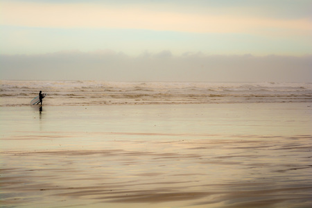 A surfer carries a surf board on the shoreline of the beachの写真素材