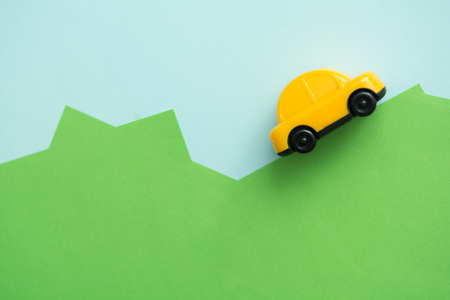 Yellow car driving over hills with blue sky backgroundの写真素材