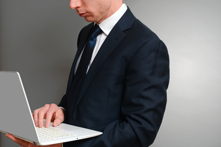 Man in a suit typing whilst holding a laptop computerの写真素材