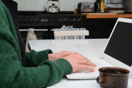 A woman using a laptop computer sitting at home at a kitchen tableの写真素材