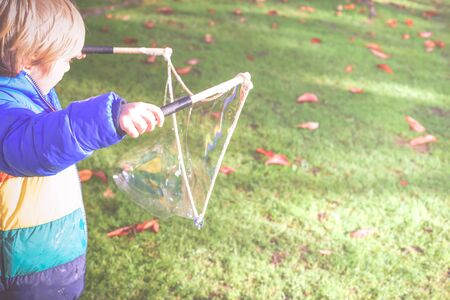 Child playing outside in a garden during day time with bubbles he is happy and runningの写真素材